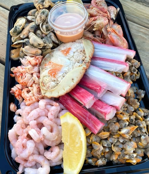 Black tray with shrimp, crab legs, clams, crab shell, lemon wedge, and dipping sauce