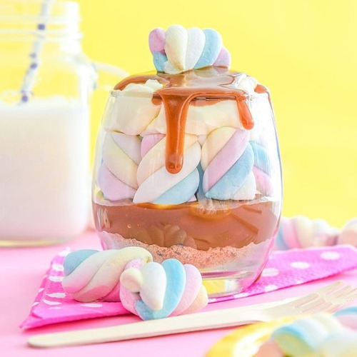 Glass jar filled with pastel marshmallows drizzled with caramel sauce on pink surface