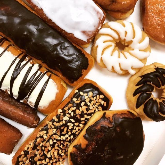 Assorted eclairs and cream puffs with chocolate, white icing, and nut toppings arranged on white background