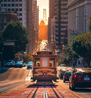 Cable car on San Francisco street with Bay Bridge illuminated by sunset in background