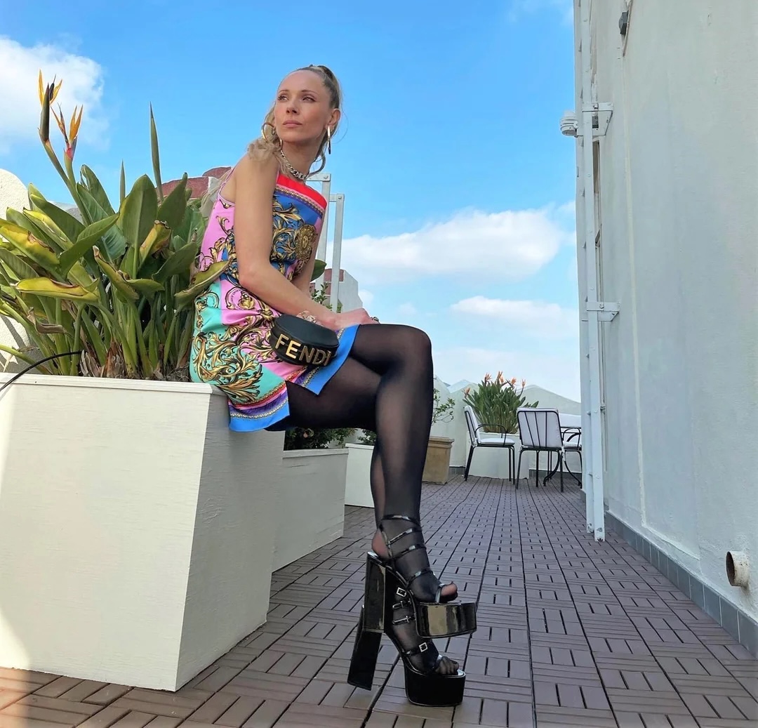 Woman in colorful dress sitting on white planter on rooftop terrace with blue sky background