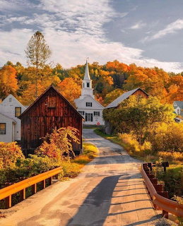 New England village with red barn, white church, and colorful autumn foliage along a road