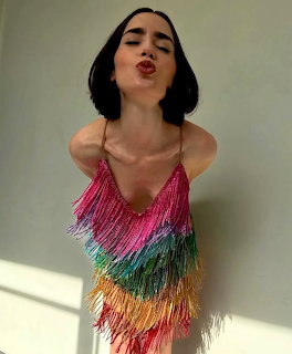 Woman with short black bob hair blowing a kiss wearing a colorful rainbow fringe top