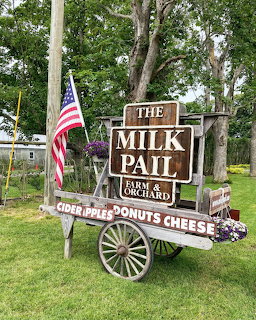 Wooden farm market cart with The Milk Pail sign and American flag on grass with trees in background