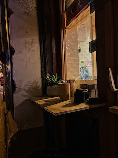 Small wooden table by a cafe window with a potted plant, cup, and warm indoor lighting