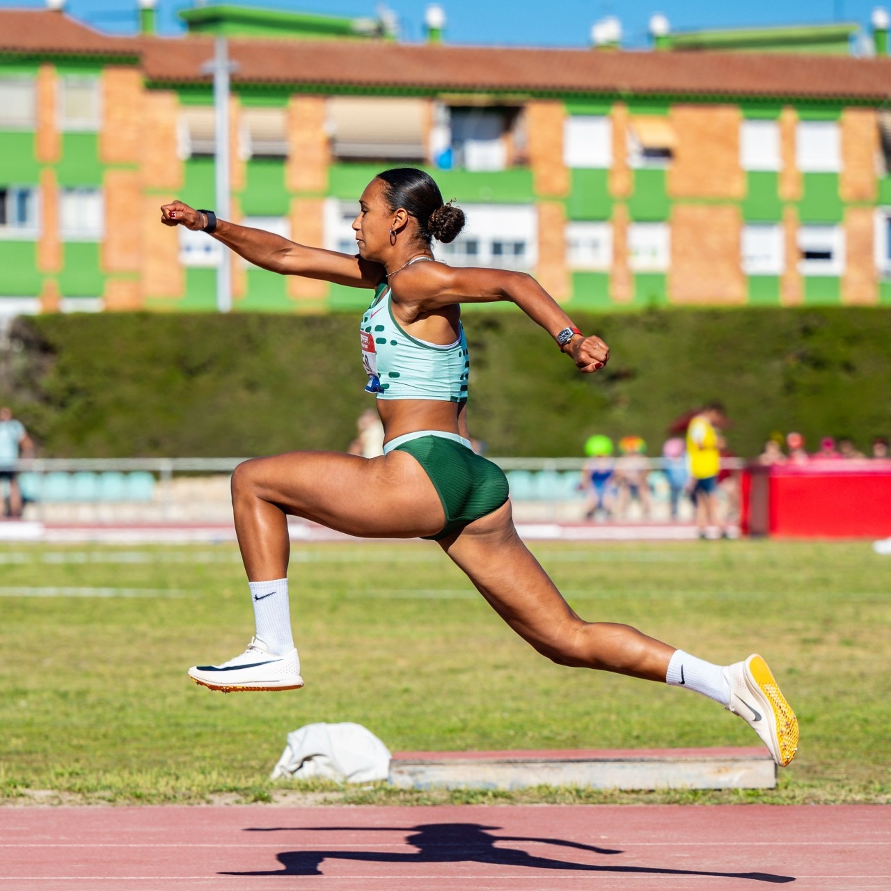 Female track athlete mid-jump on a sports field in side view