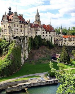 Sigmaringen Castle on a cliff above a river with green trees and historic town buildings