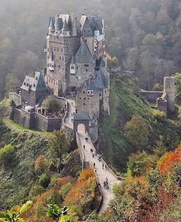 Burg Eltz medieval castle on a hill amid autumn-colored trees and mist