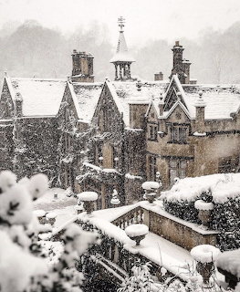Snow-covered rooftops of an old stone manor house with chimneys during heavy snowfall