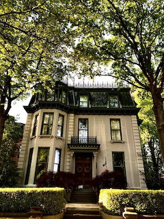 Victorian house with bay windows framed by trees and hedges