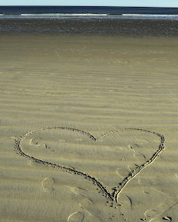 Heart shape drawn in sand on a beach with ocean and dark sky in the background