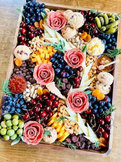 Top-down hors d'oeuvres platter with fruit, cheese, crackers, dips, and rose-shaped salami