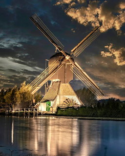 Dutch windmill beside water at sunset with dramatic cloudy sky
