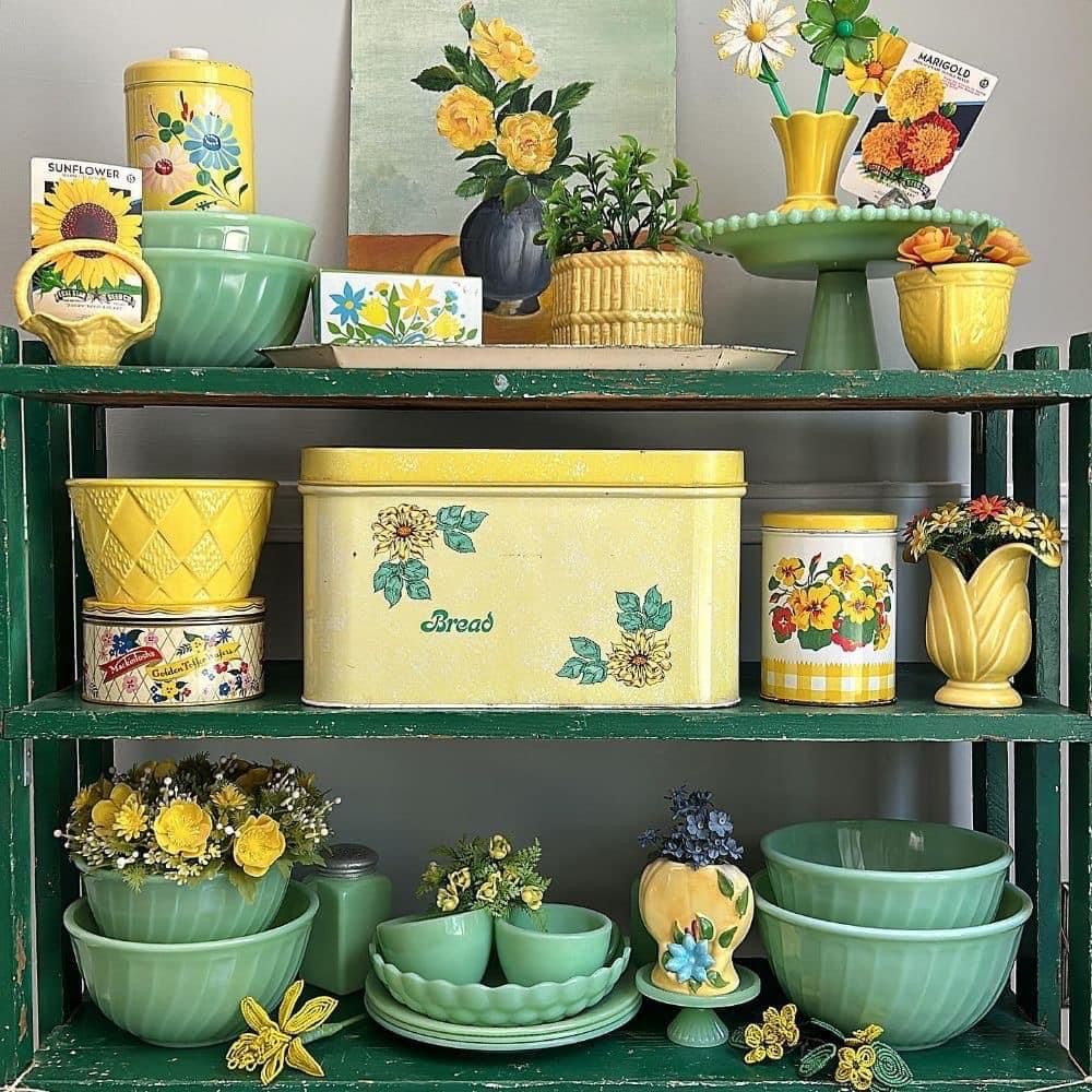 Vintage yellow and green bowls, tins, and flower vases arranged on dark green shelves