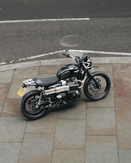 Black Triumph scrambler motorcycle parked on stone pavement, aerial view