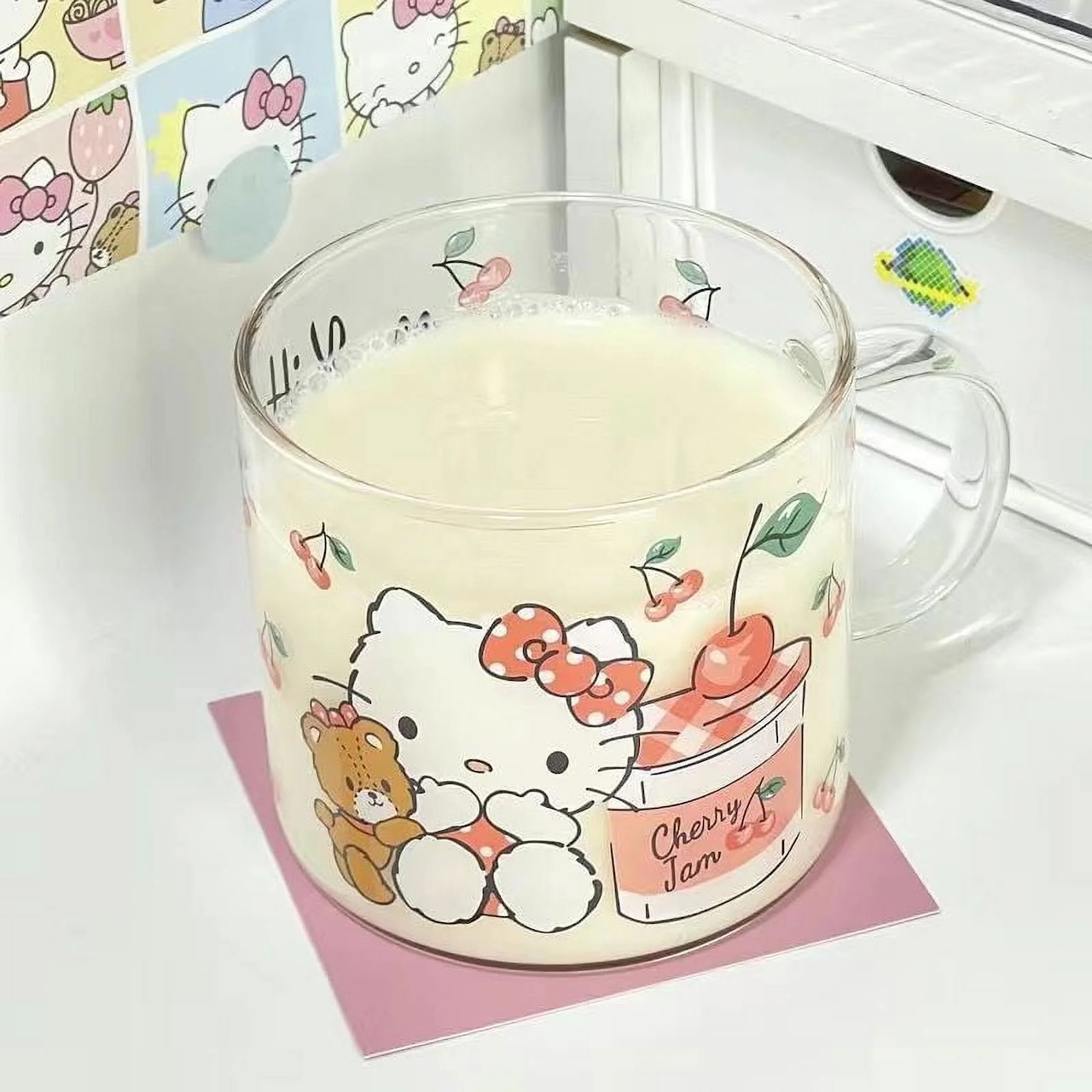 Glass mug decorated with Hello Kitty and teddy bear design, filled with milk, placed on pink coaster