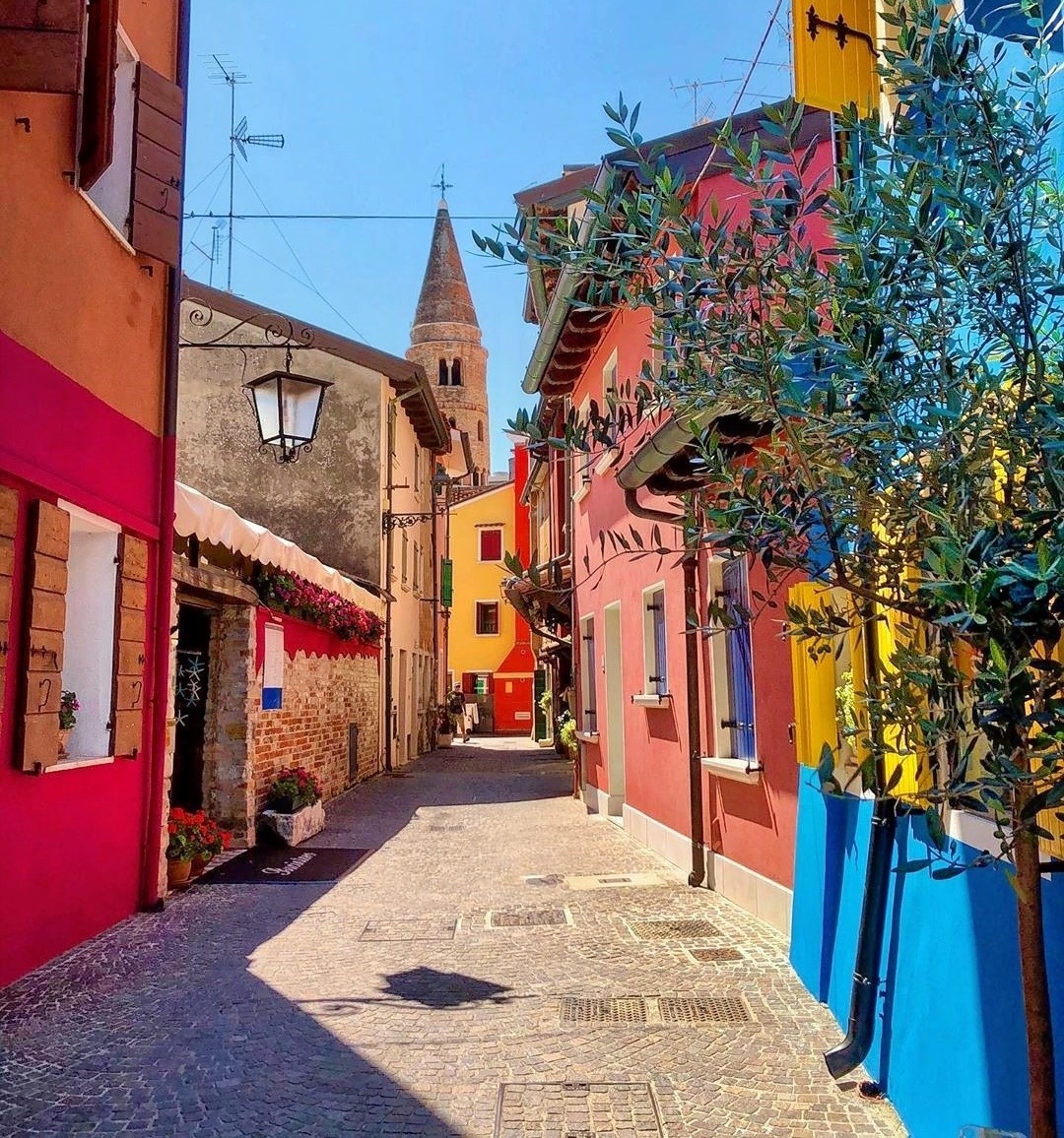 Narrow cobblestone street with colorful houses and a bell tower in Caorle