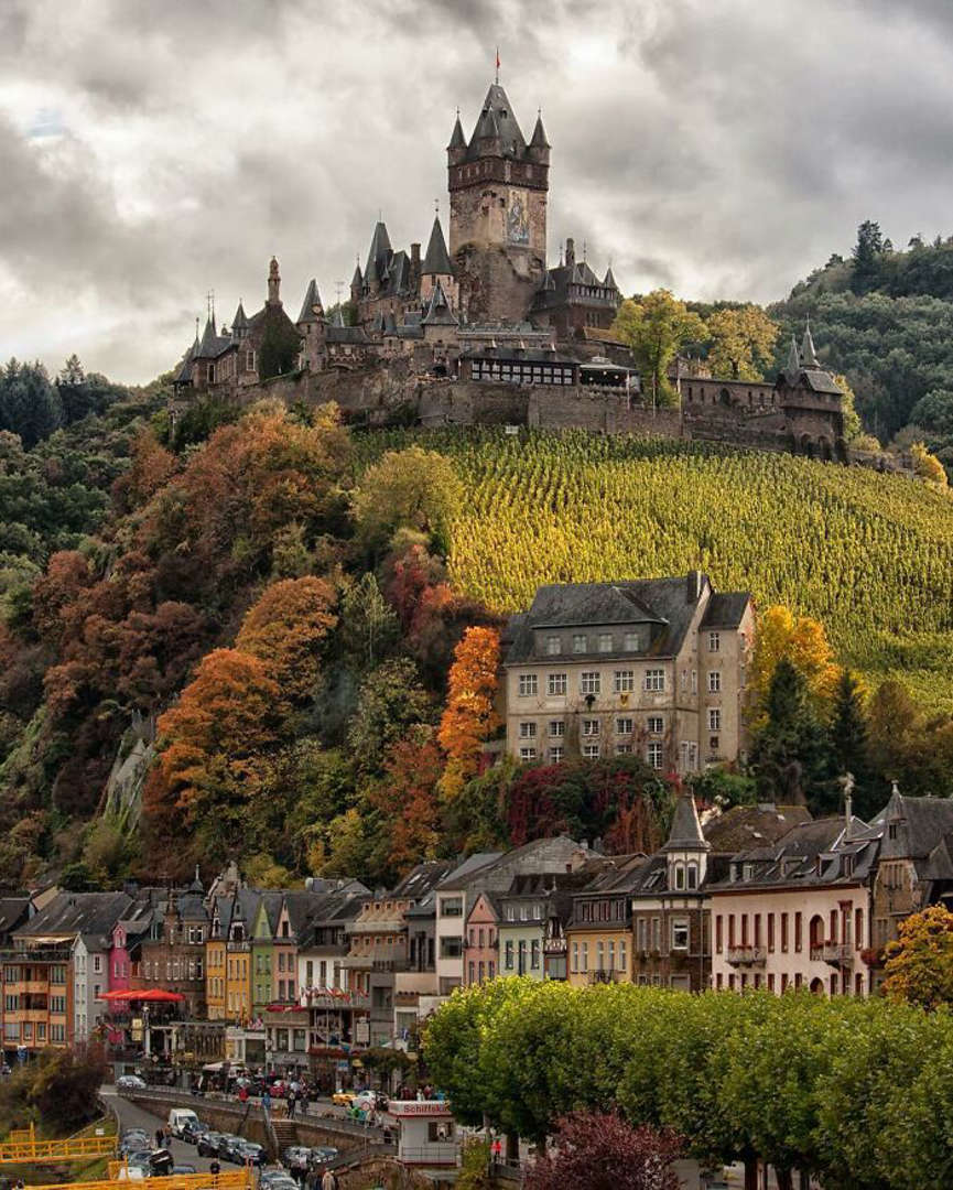 Cochem Castle towering over village with autumn vineyards and colorful trees on hillside