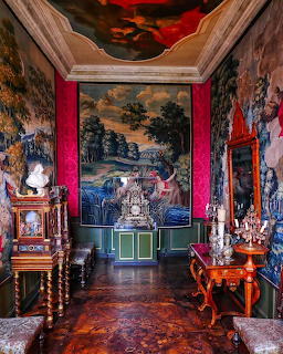 Lavish palace interior with red walls, ceiling fresco, landscape painting, ornate furniture and chandeliers