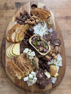 Charcuterie board with salami, cheese slices, bread, walnuts, olives, and herbs on a wooden platter