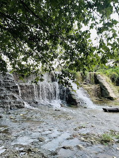 Waterfall flowing over a stone dam at Veteran's Park, Round Rock, Texas, framed by green tree branches