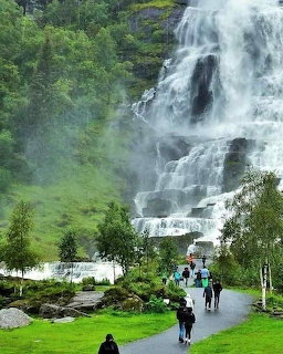 Large cascading waterfall on a green hillside with visitors walking on a path below
