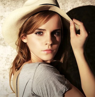 Young woman with light brown hair wearing a straw hat and grey shirt, hand on hat brim