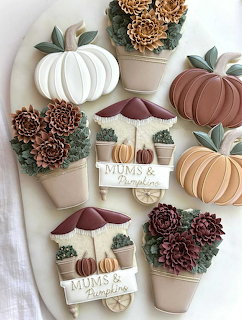 Decorated fall sugar cookies shaped like pumpkins, poted mums, and flower arrangements in autumn colors