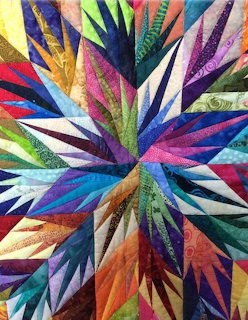 Vibrant quilt with radiating star pattern in multiple bright colors and geometric fabric pieces