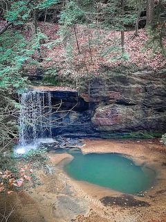 Waterfall flowing over sandstone ledge into turquoise pool surrounded by autumn trees and rocks