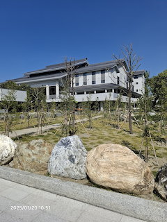 Modern building with landscaped garden, large rocks, young trees, and green lawn under blue sky