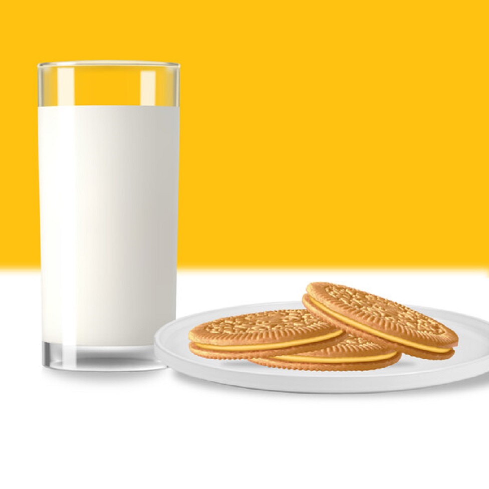 Glass of milk next to a plate of sandwich cookies on a yellow background