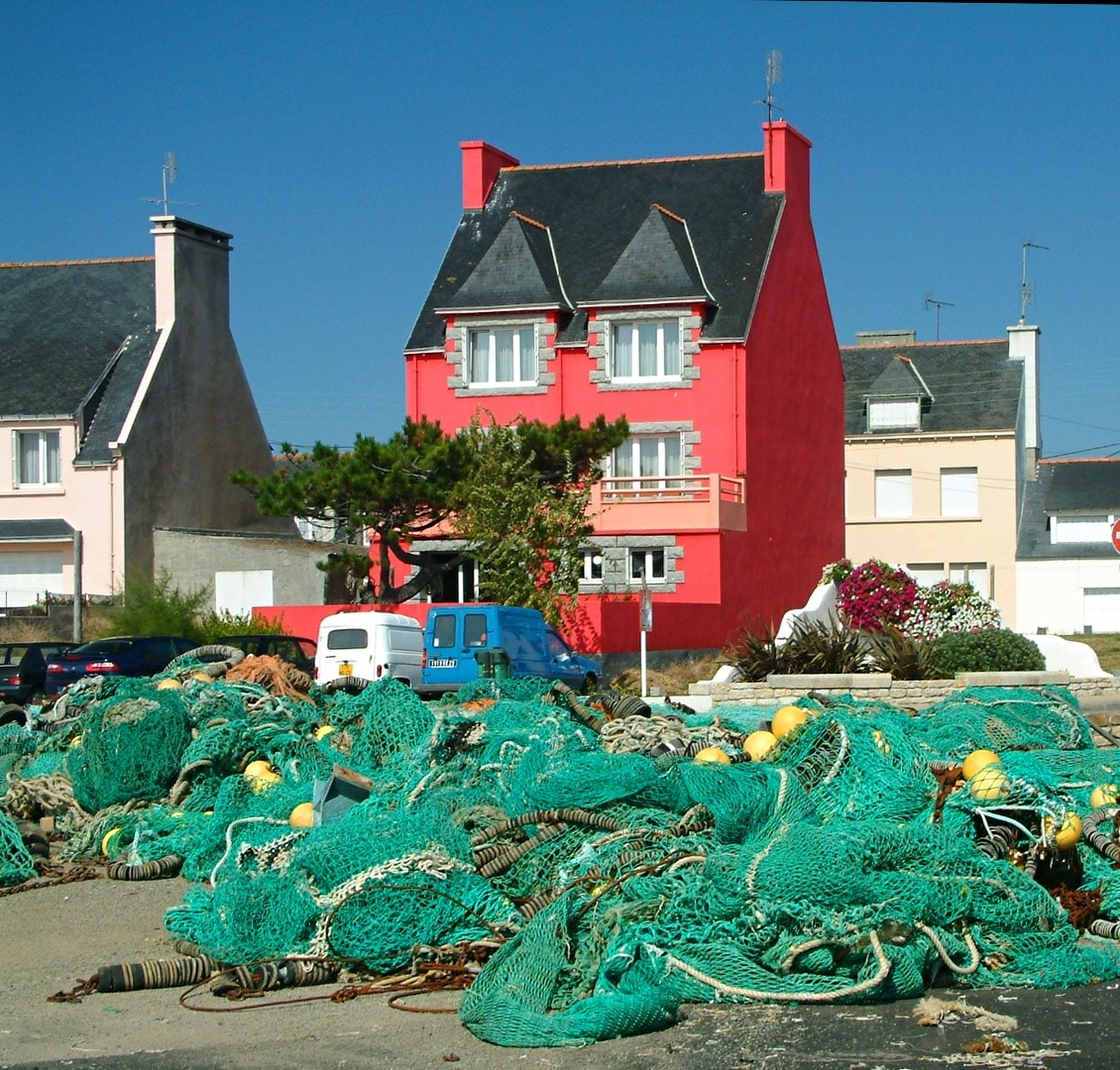 Green fishing nets in front of a bright red house and nearby homes under a blue sky