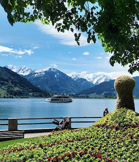 Passenger boat on mountain lake with snow peaks and garden sculpture framed by tree branches