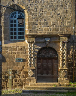 Ornate wooden doorway in a stone chapel wall with twisted columns and a tall arched window