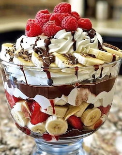 Layered trifle dessert in glass bowl with berries, bananas, whipped cream, and chocolate drizzle