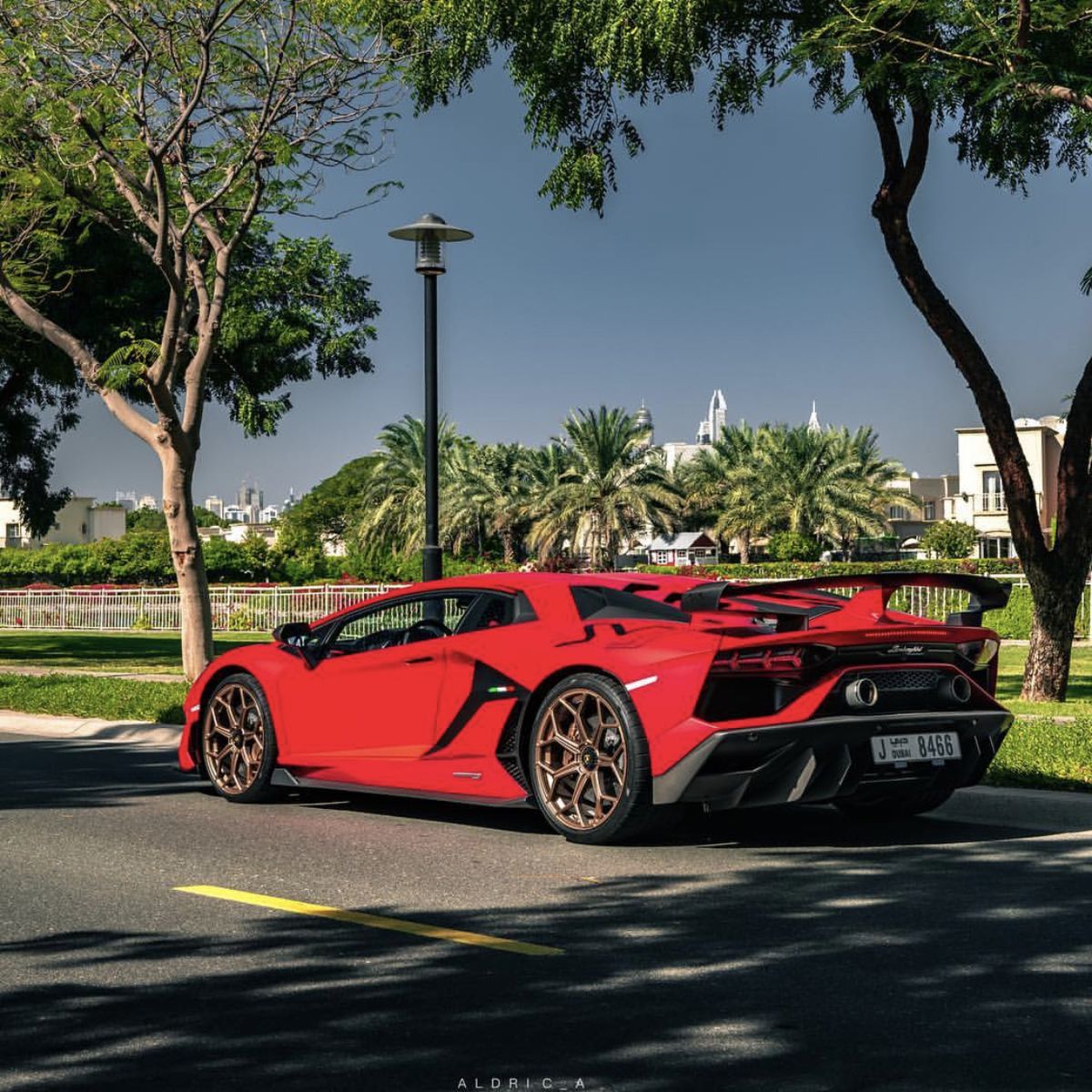 Red Lamborghini Aventador sports car parked on urban street with palm trees
