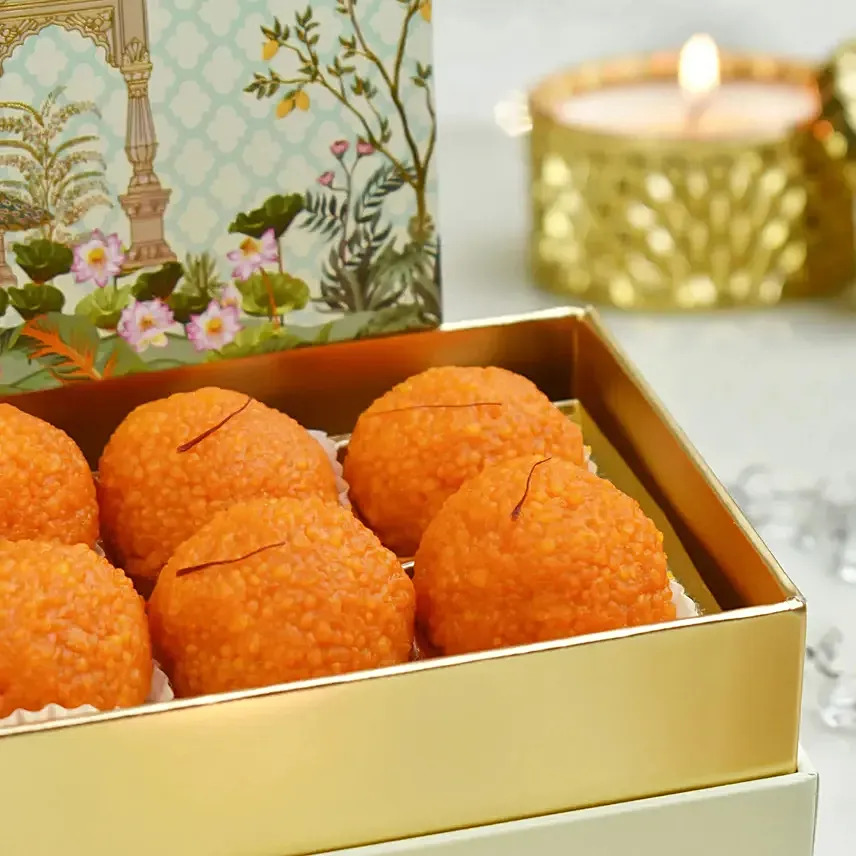 Orange ladoo sweets in a gold box with a lit candle and decorative backdrop