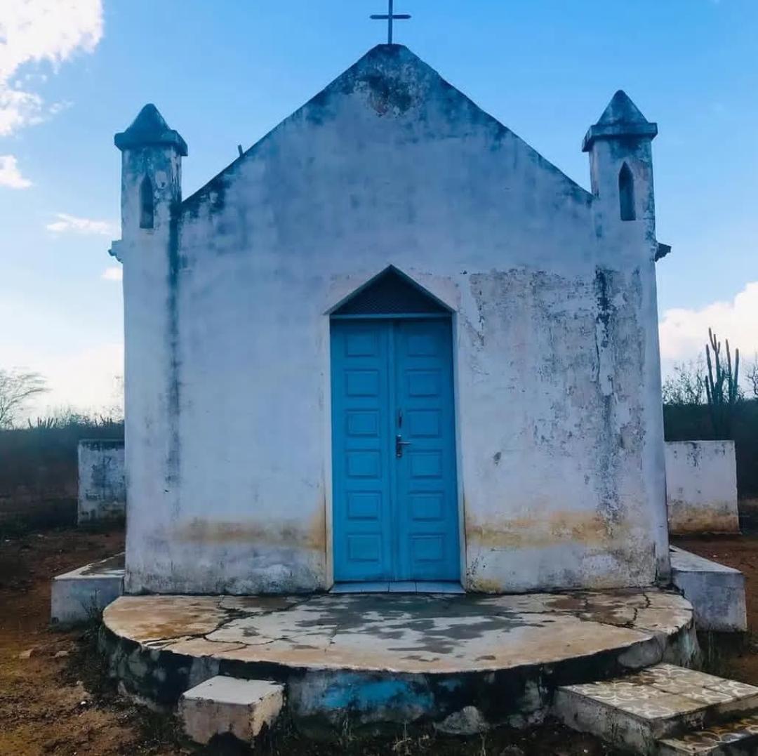 Front view of a small old white chapel with a blue door and twin bell towers