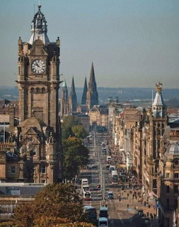 Historic clock tower overlooking a busy street in Edinburgh with church spires in the distance.