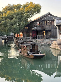 Traditional wooden boats mored on green canal in historic Chinese water town with traditional architecture