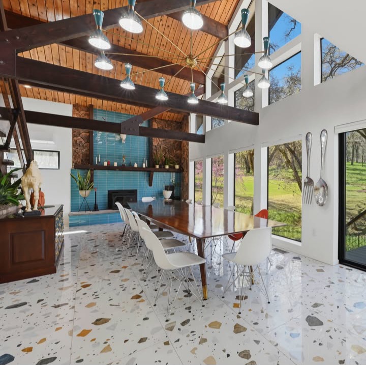 Bright modern loft interior with dining table, white chairs, blue tiled fireplace, and large windows