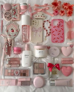 Flatlay of pink beauty products, makeup palettes, skincare bottles, and accessories arranged aesthetically on white surface