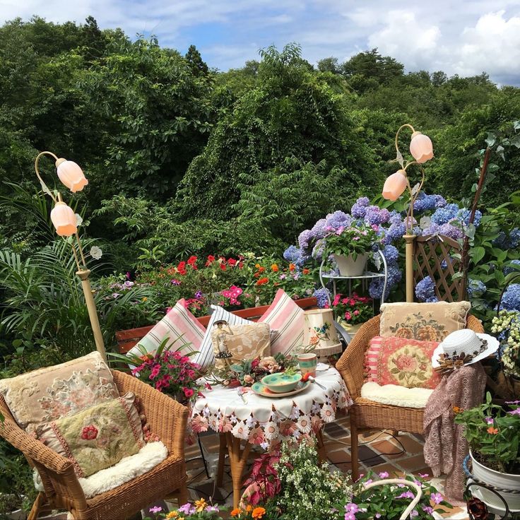 Wicker chairs and a floral table in a lush garden with blooming flowers and greenery