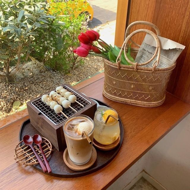 Cafe tray with dango on a grill, iced latte, yuzu drink, woven basket, and tulips by a window
