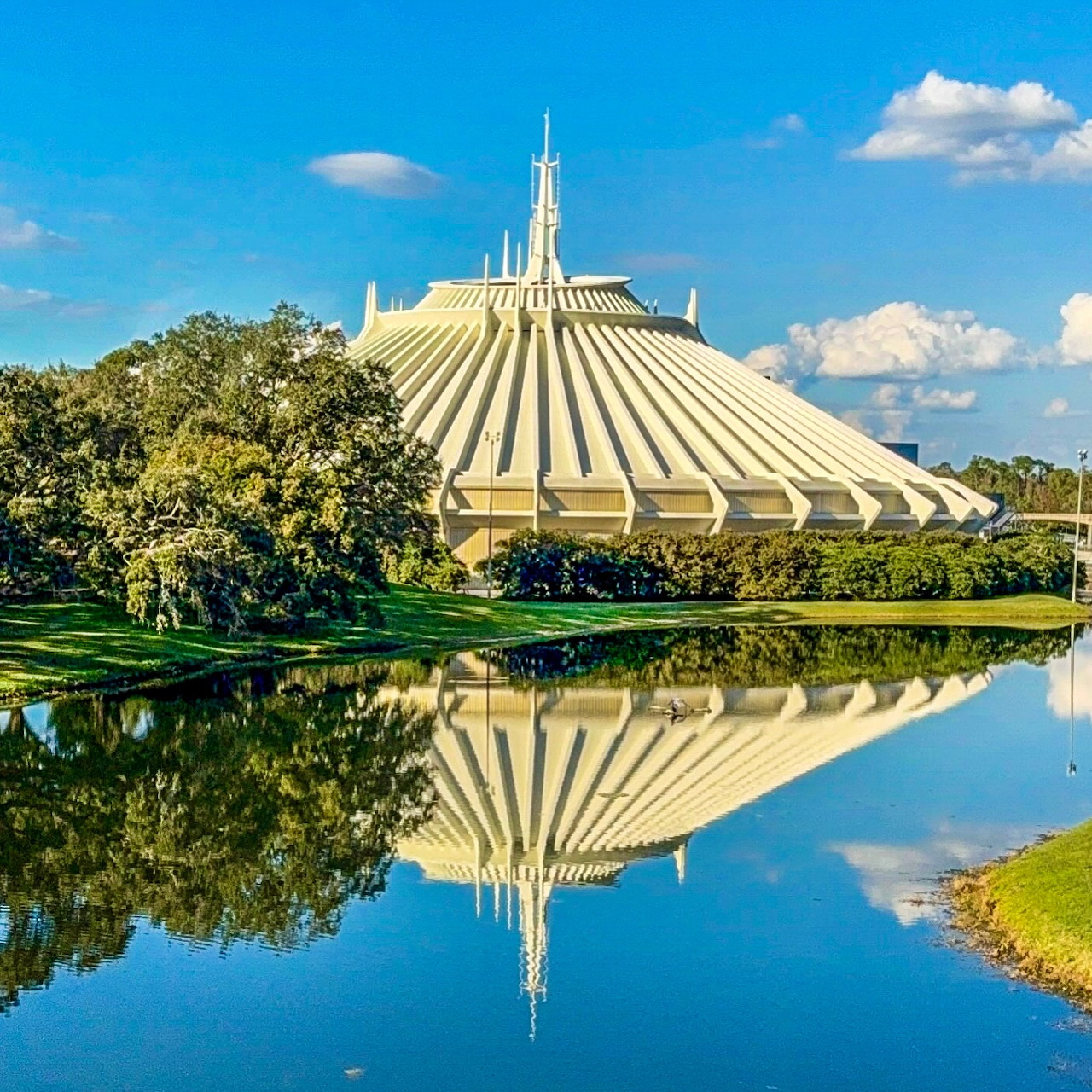 Space Mountain white cone building reflected in pond with trees and blue sky
