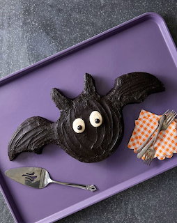 Bat-shaped chocolate cake with candy eyes on a purple tray beside a fork and checkered napkins