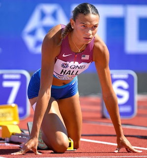 Female sprinter in crouch start position on red track wearing maroon and blue uniform