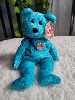 Blue TY Beanie Baby bear plush sitting on a white blanket
