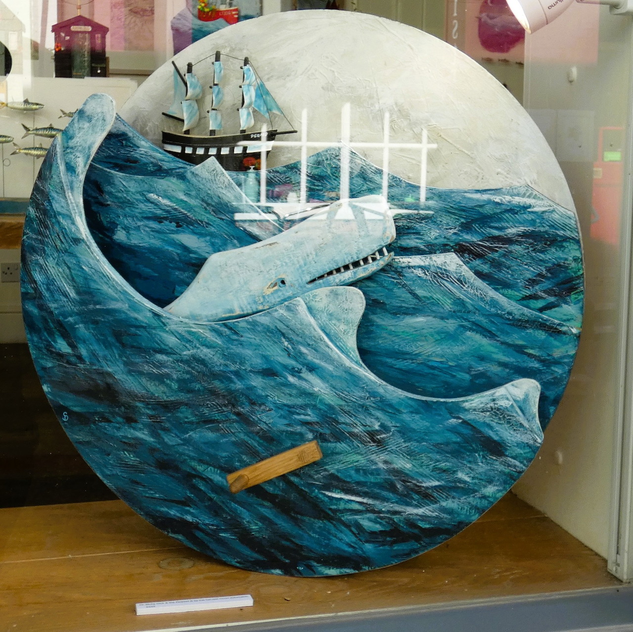 White whale breaching blue ocean waves with sailing ship, Moby-Dick themed circular artwork